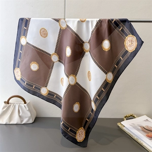 Macro detail of silk scarf featuring checkered pattern with gold chain and lion emblem