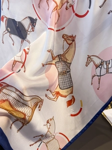 Detail of silk-like scarf featuring equestrian horse prints and navy blue rolled edges