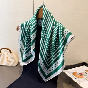 Elegant green and white polka dot silk-like scarf draped on a wooden hanger stylishly