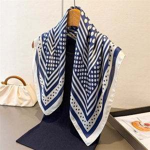 Navy and white polka dot silk-like square scarf draped over a wooden hanger