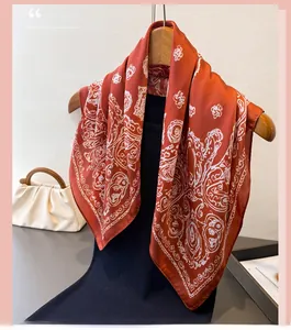 Detail of caramel silk scarf with white paisley pattern draped on a wooden hanger