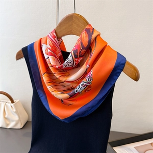 Detail of silk scarf featuring equestrian prints and orange finish on a black knit top