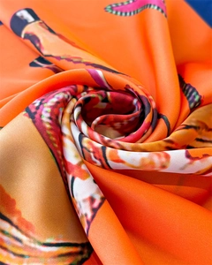 Detailed macro view of vibrant orange equestrian print silk scarf with satin texture and drape