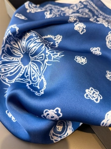 Detail shot of navy blue silk-like scarf featuring elegant white floral paisley patterns