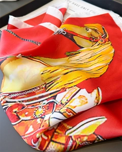 Detail of red silk scarf with equestrian horse print folded on a black display tray
