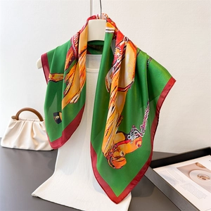 Equestrian print silk-like green square scarf with red edges hung on a white knit vest