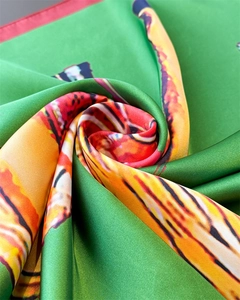 Detailed macro view of green silk satin scarf with vibrant orange abstract patterns