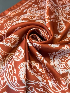 Close-up of rust red silk scarf featuring white paisley pattern and smooth satin texture