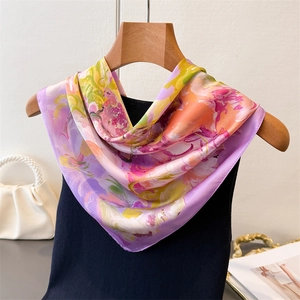 Detailed shot of floral silk square scarf in purple and orange on a wooden hanger