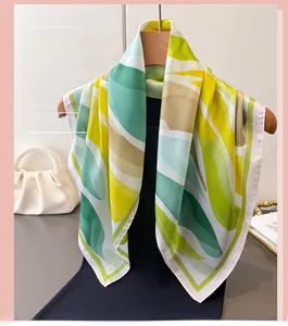 Gros plan d'un foulard carré en soie avec des motifs de feuilles vertes et jaunes