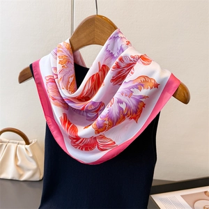 Detailed view of floral silk scarf tied to a black vest with vibrant feather pattern