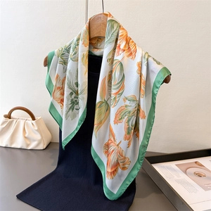 Elegant silk-like scarf with green and orange tulip patterns on a hanger with a stylish bag