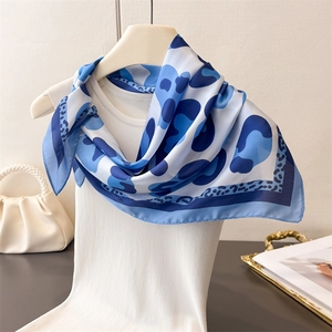 Detail of blue abstract leopard print silk scarf draped on a white knitted top