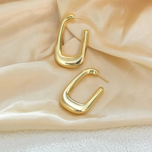 Close-up of golden U-shaped earrings with mirror finish on champagne satin fabric