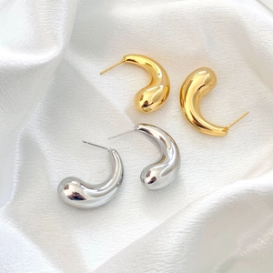 Polished 18K gold and silver teardrop earrings displayed on elegant white silk fabric
