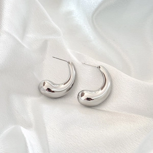 Polished silver geometric drop earrings on white satin background with mirror finish