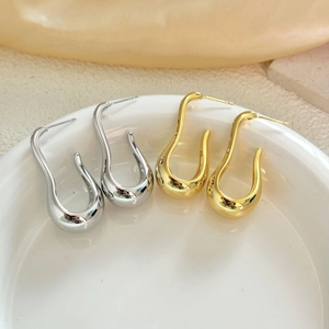 Polished U-shaped teardrop hoop earrings in gold and silver finish on a ceramic tray