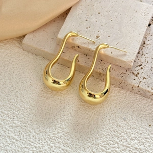 Detailed view of glossy gold U-shape earrings on white stone and satin silk background