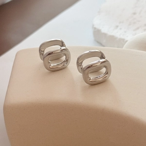 Minimalist double oval silver earrings on a beige pedestal with a natural stone background