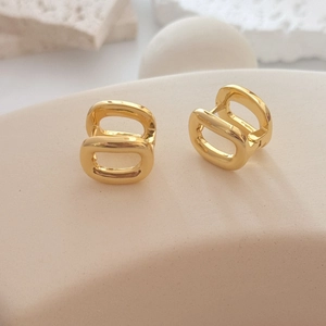 Minimalist double oval gold earrings with polished finish on a warm beige pedestal