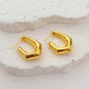 Minimalist geometric hexagon earrings in polished gold on white stone blocks display