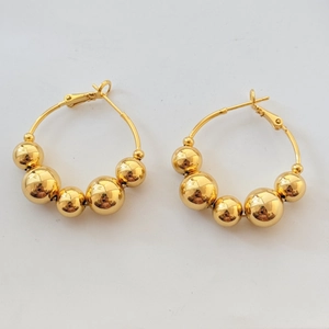 Detail view of gold hoop earrings with polished beads on white background