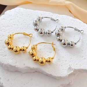 Detail view of 18K gold and silver plated beaded hoop earrings on a stone background