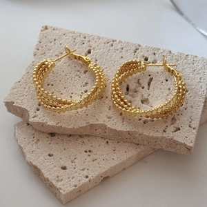 Goldene dreilagige Perlen-Creolen mit strukturierter Oberfläche auf beigem Stein