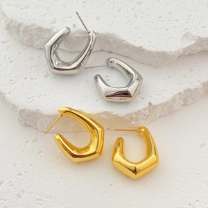 Minimalist geometric hollow earrings in gold and silver finish on textured stone surface