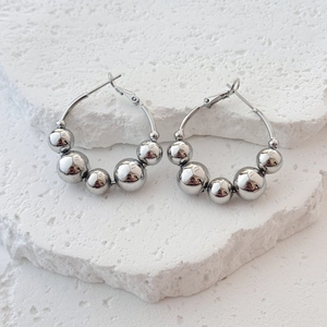 Polished silver metal hoop earrings with graduated beads on white stone base