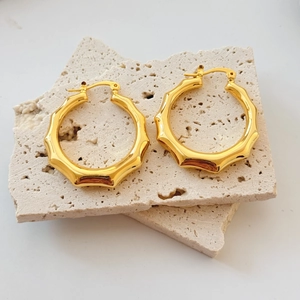 Détail de boucles d'oreilles géométriques creuses en or 18 carats sur pierre texturée
