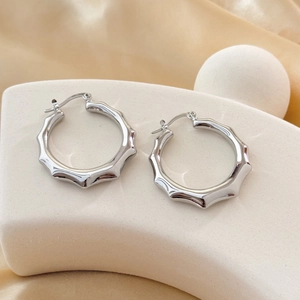 Boucles d'oreilles créoles argentées style bambou sur support d'exposition blanc