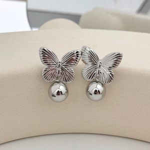 Boucles d'oreilles papillon argentées avec sphère métallique sur présentoir beige