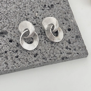 Irregular textured silver double hoop earrings displayed on a grey volcanic rock base