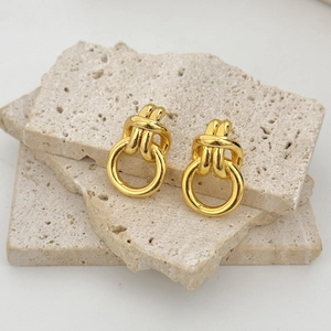 Polished golden knot drop earrings displayed on natural travertine stone background