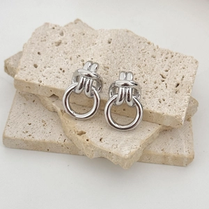 Minimalist silver knot drop earrings with round pendant on white travertine stone