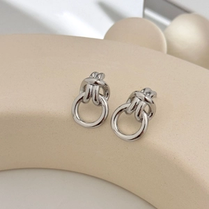 Close-up of silver metal knot earrings with hanging hoop on beige geometric stand