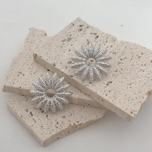 Minimalist silver sunburst stud earrings with frosted metal texture on beige stone