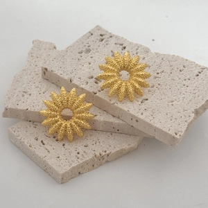 Matte gold sunflower stud earrings with textured finish on natural travertine stone