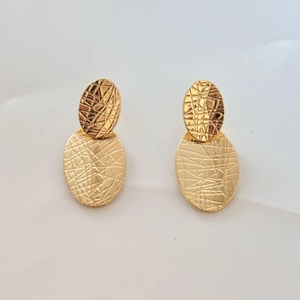 Close-up of golden oval double-layer earrings with geometric textured pattern design