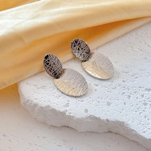 Silver geometric oval earrings with engraved textured finish on textured stone background