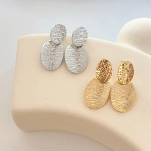 Detailed view of layered oval metal earrings with rock texture in gold and silver