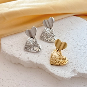 Detailed shot of gold and silver heart earrings on a natural stone and silk backdrop