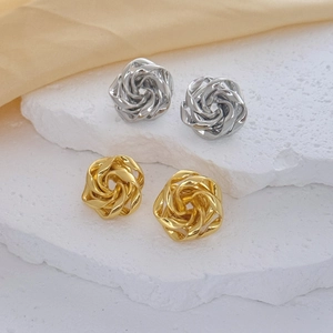 Detailed view of 3D rose stud earrings in gold and silver on a white stone display