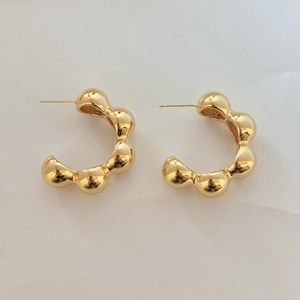 Close-up of golden bubble beaded C-shaped earrings with wave texture and mirror finish