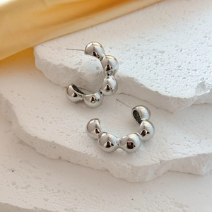 Polished silver beaded C-shaped hoop earrings on a textured white stone display