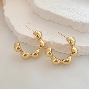 Macro detail of golden C-shaped bubble earrings with polished finish on textured stone