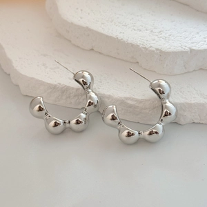 Macro view of silver geometric C-shape bubble earrings on a white marble stone stand