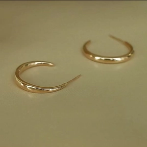 Detail of C-shaped gold hoop earrings featuring a minimalist mirror-polished surface