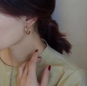 Minimalist round gold earrings with a polished finish worn by a model in a side view